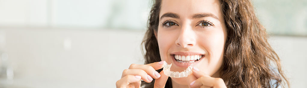 woman inserting clear aligners onto her teeth