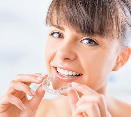 woman inserting clear aligners onto her teeth