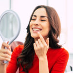 Photograph of a woman smiling at herself in the mirror after finishing cosmetic dentistry.