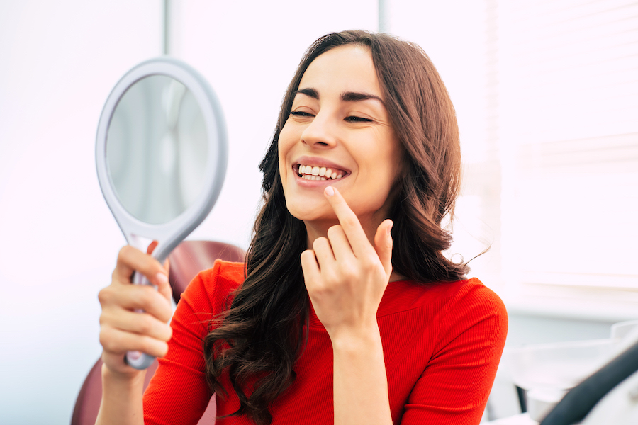 Photograph of a woman smiling at herself in the mirror after finishing cosmetic dentistry.
